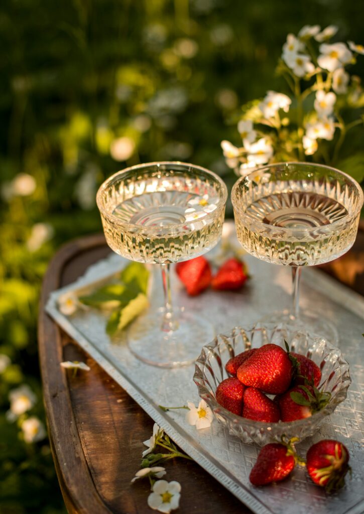 Vassoio di metallo con coppia di bicchieri da champagne in cristallo molato, i bicchieri sono pieni e vengono accompagnati da fragole